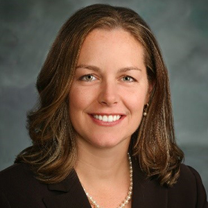 Dr. Jill A. Rough stands smiling while wearing a black suit and yellow shirt.