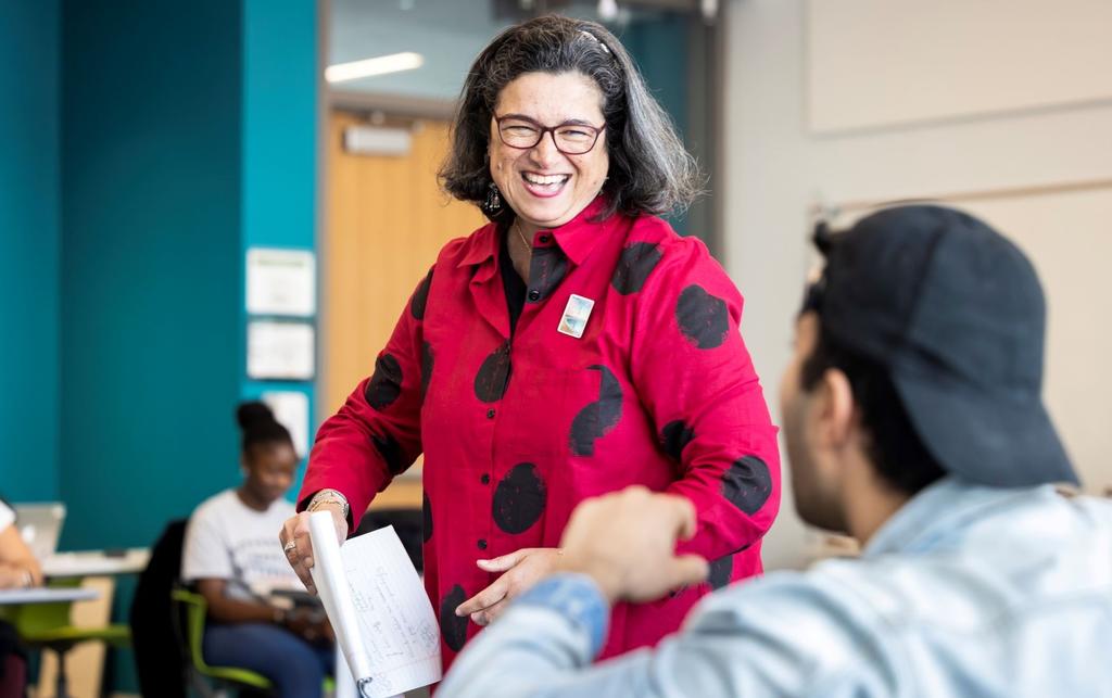 Professor wearing a red and black polka dot shirt smiles at a student during class.